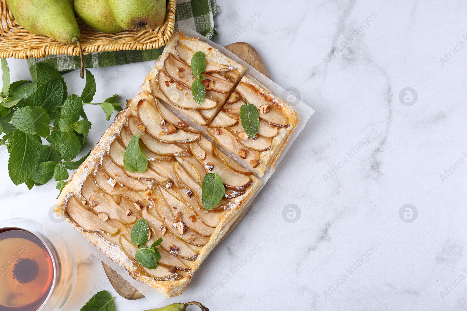 Photo of Tasty puff pastry pie with pears, mint and tea on white marble table, top view. Space for text