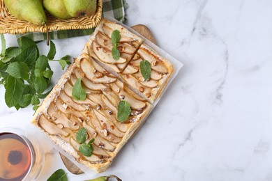 Photo of Tasty puff pastry pie with pears, mint and tea on white marble table, top view. Space for text