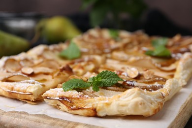 Photo of Tasty puff pastry pie with pears and mint on board, closeup