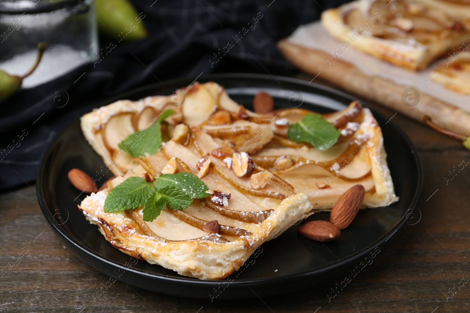 Photo of Pieces of tasty puff pastry pie with pears, mint and almonds on wooden table, closeup