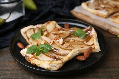 Photo of Pieces of tasty puff pastry pie with pears, mint and almonds on wooden table, closeup