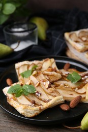 Photo of Pieces of tasty puff pastry pie with pears, mint and almonds on wooden table, closeup