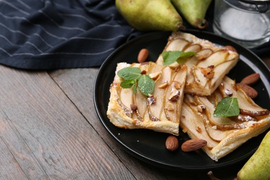 Pieces of tasty puff pastry pie with pears, mint and almonds on wooden table, closeup