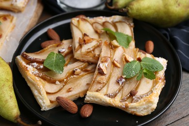 Photo of Pieces of tasty puff pastry pie with pears, mint and almonds on wooden table, closeup