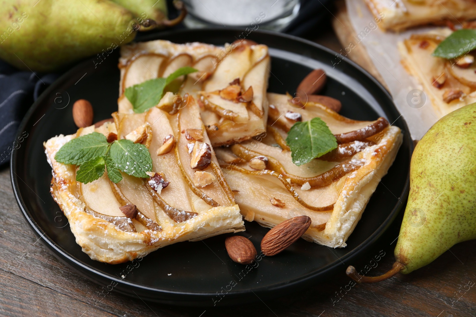 Photo of Pieces of tasty puff pastry pie with pears, mint and almonds on wooden table, closeup