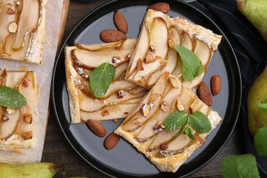 Photo of Pieces of tasty puff pastry pie with pears, mint and almonds on wooden table, top view