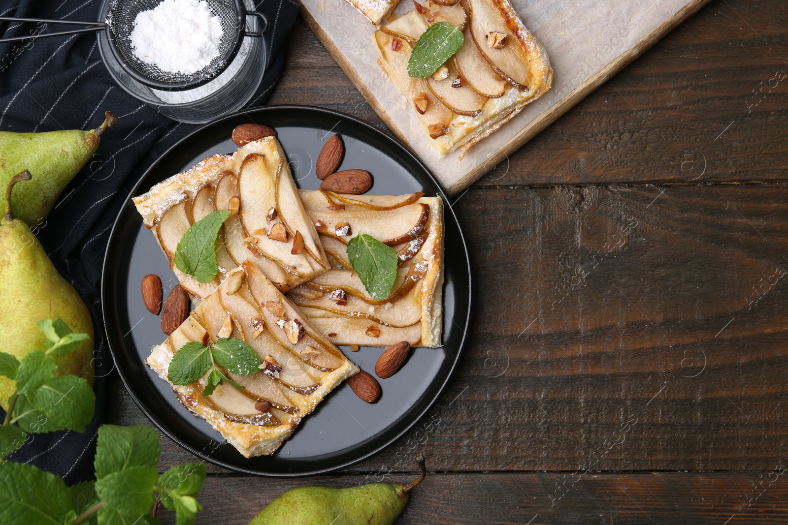 Photo of Pieces of tasty puff pastry pie with pears, mint and almonds on wooden table, top view. Space for text