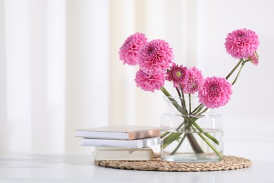 Photo of Beautiful pink flowers in vase and books on table indoors. Space for text