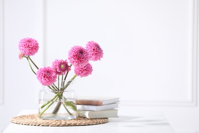 Photo of Beautiful pink flowers in vase and books on table indoors. Space for text