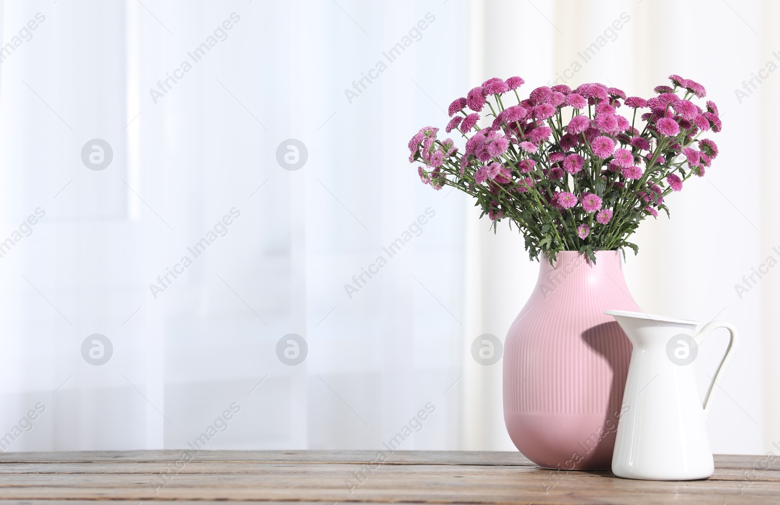 Photo of Beautiful pink flowers in vase on wooden table indoors. Space for text