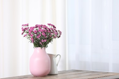 Photo of Beautiful pink flowers in vase on wooden table indoors. Space for text