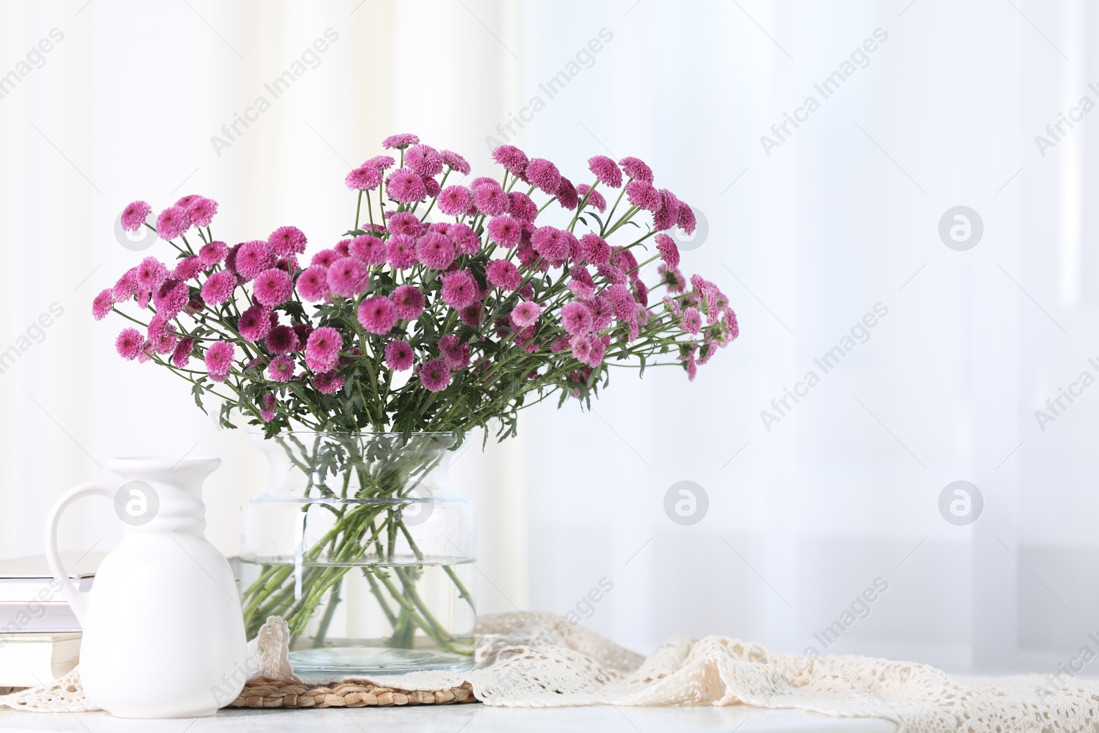 Photo of Beautiful pink flowers in vase and books on table indoors. Space for text