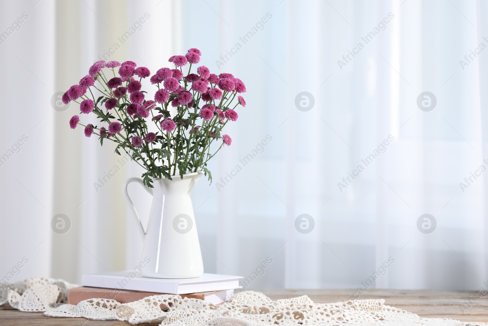 Photo of Beautiful pink flowers in vase and books on table indoors, space for text