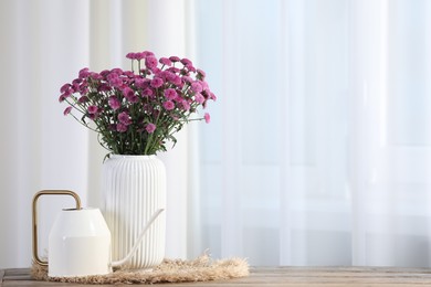 Photo of Beautiful pink flowers in vase and watering can on wooden table indoors. Space for text