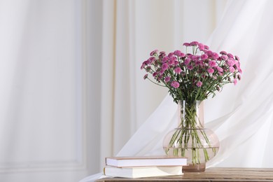 Photo of Beautiful pink flowers in vase and books on table indoors, space for text