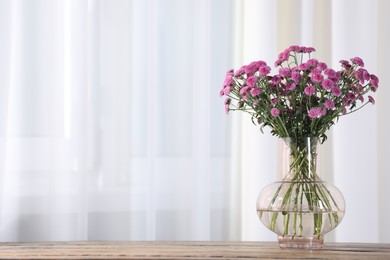 Photo of Beautiful pink flowers in vase on table indoors. Space for text