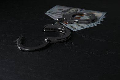 Photo of Corruption. Dollar banknotes and handcuffs on black table