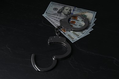 Photo of Corruption. Dollar banknotes and handcuffs on black table