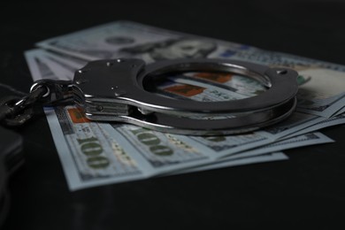 Photo of Corruption. Dollar banknotes and handcuffs on black table, closeup