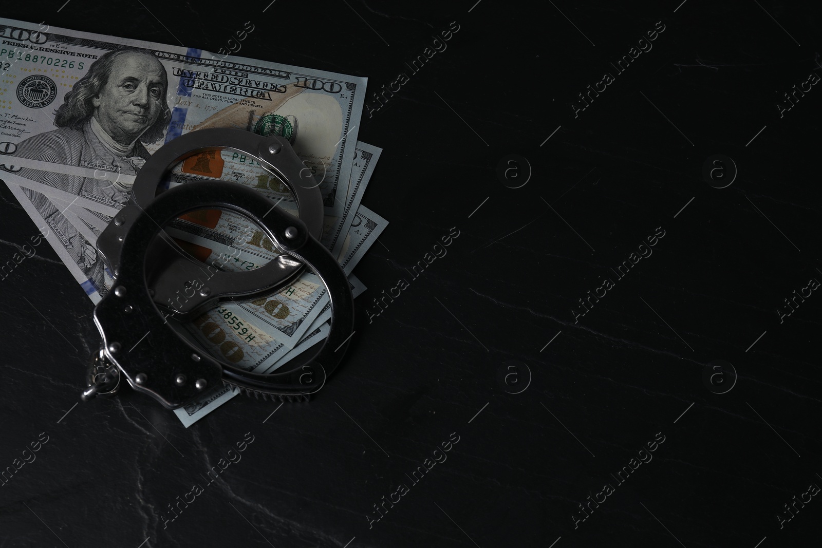 Photo of Corruption. Dollar banknotes and handcuffs on black table, space for text