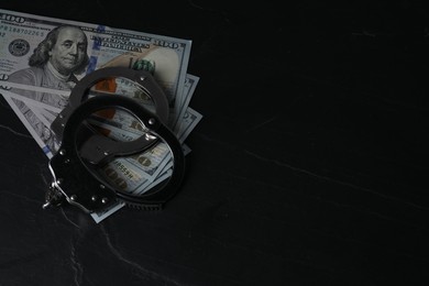 Corruption. Dollar banknotes and handcuffs on black table, space for text