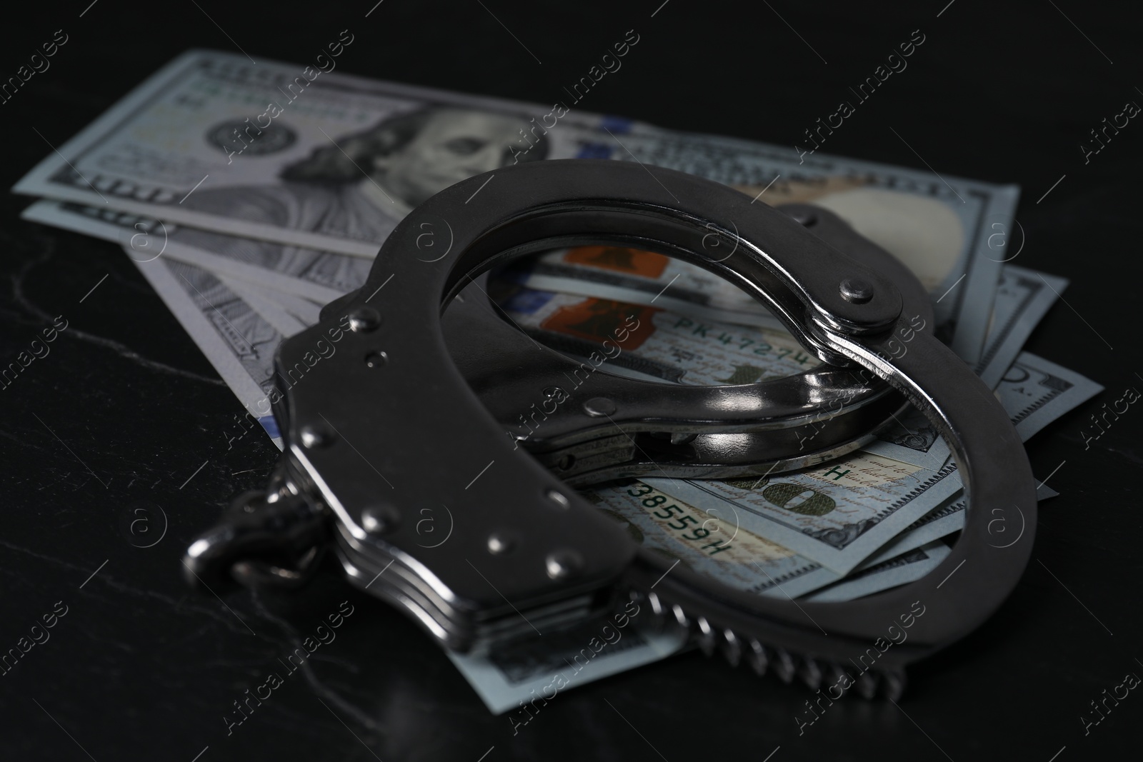 Photo of Corruption. Dollar banknotes and handcuffs on black table, closeup