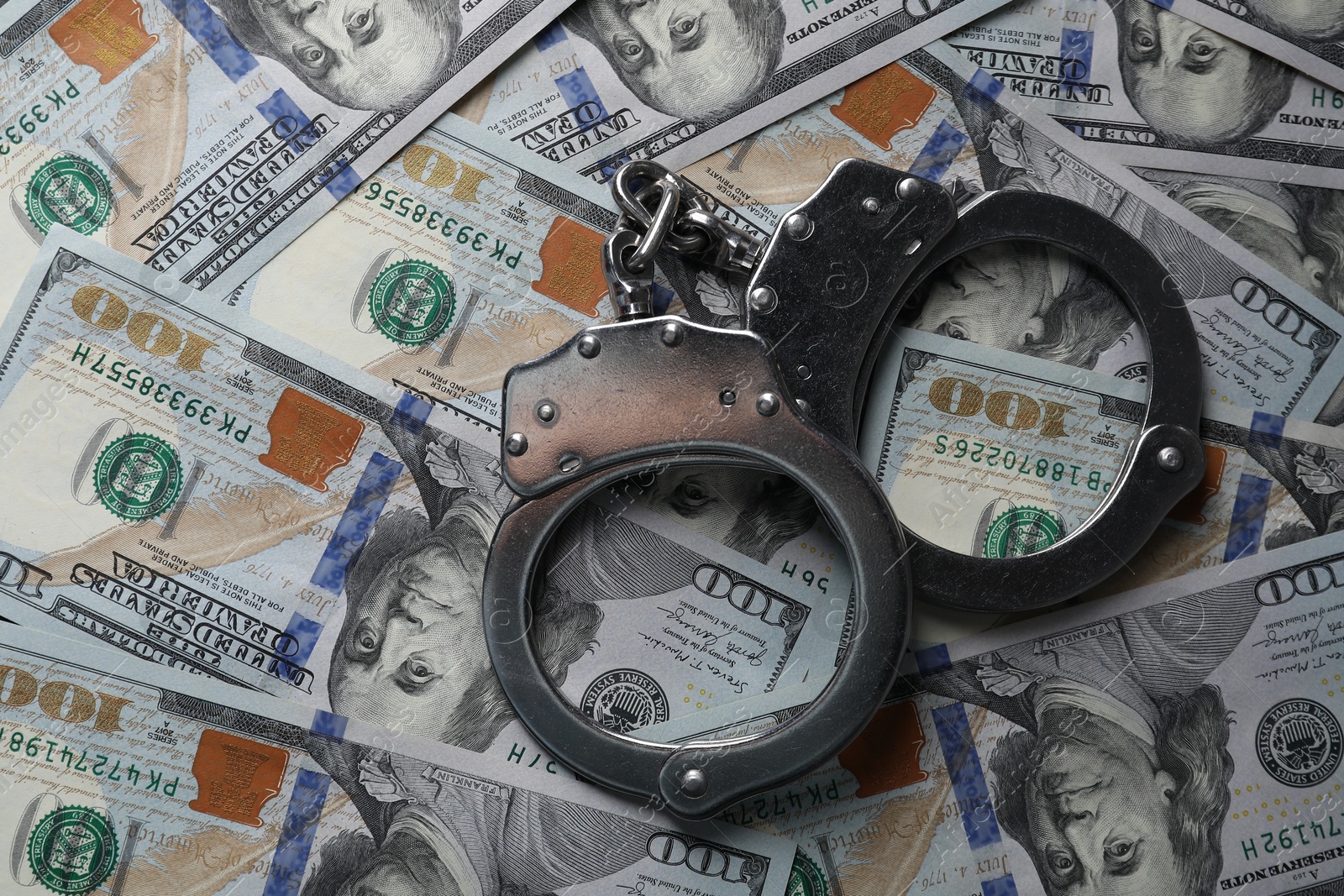 Photo of Corruption. Handcuffs on dollar banknotes, top view