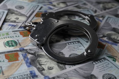 Photo of Corruption. Handcuffs on dollar banknotes, closeup view