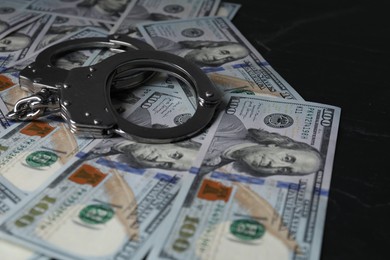 Photo of Corruption. Handcuffs and dollar banknotes on black table, closeup