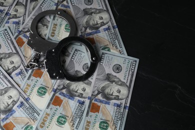 Photo of Corruption. Handcuffs and dollar banknotes on black table, top view. Space for text