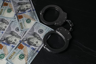 Photo of Corruption. Handcuffs and dollar banknotes on black table