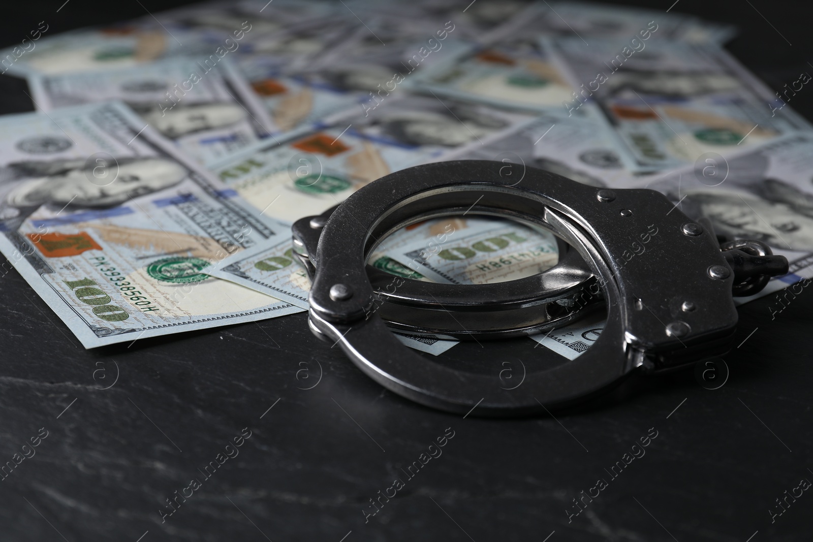 Photo of Corruption. Handcuffs and dollar banknotes on black table, closeup