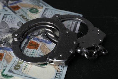 Photo of Corruption. Handcuffs and dollar banknotes on black table, closeup