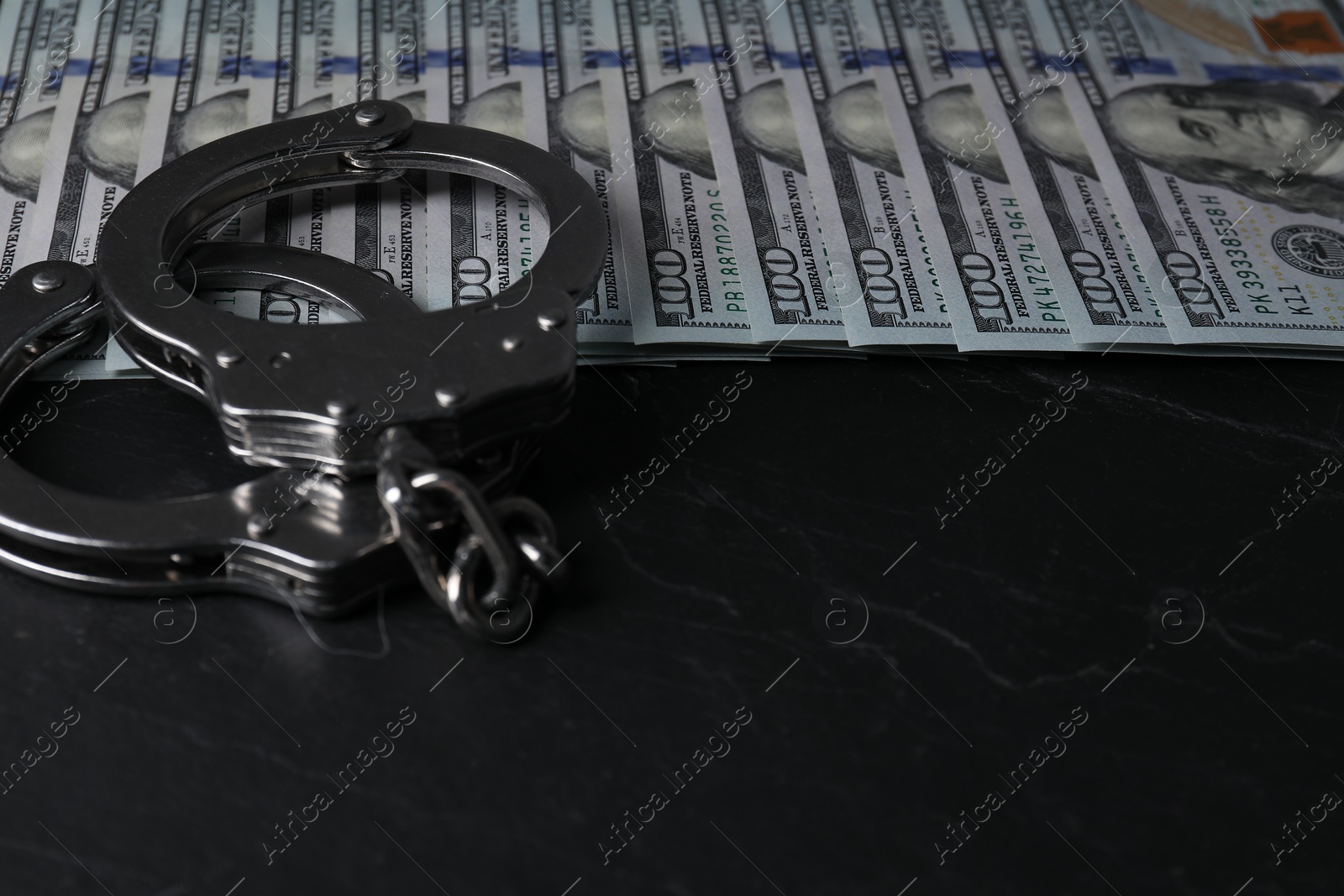 Photo of Corruption. Handcuffs and dollar banknotes on black table, closeup