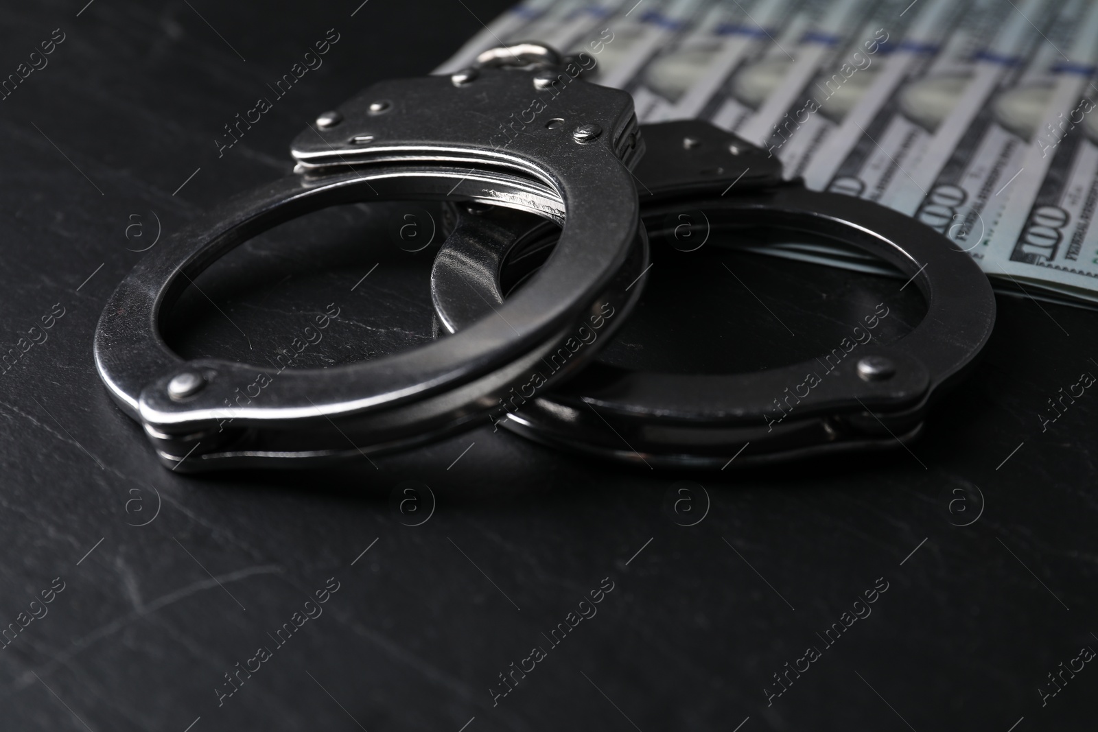 Photo of Corruption. Handcuffs and dollar banknotes on black table, closeup