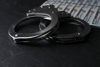 Corruption. Handcuffs and dollar banknotes on black table, closeup