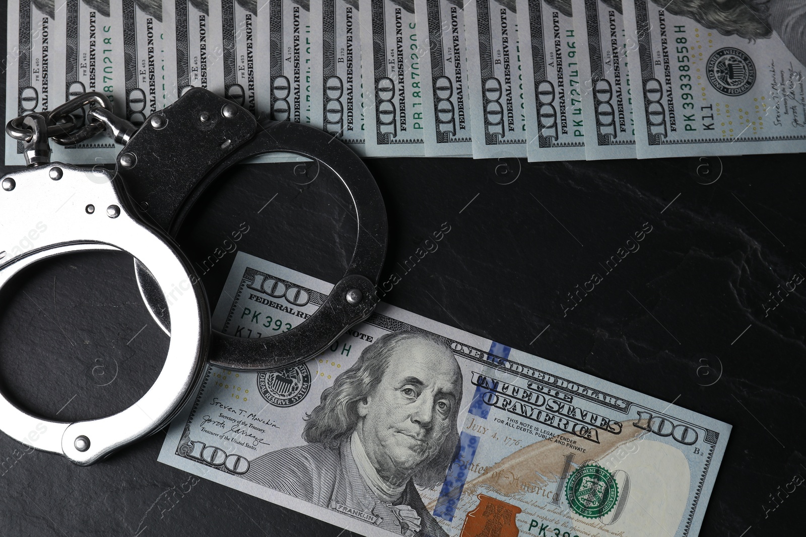 Photo of Corruption. Handcuffs and dollar banknotes on black table, flat lay