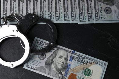 Corruption. Handcuffs and dollar banknotes on black table, flat lay