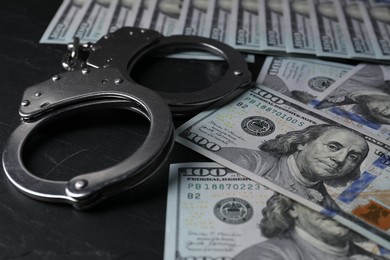 Photo of Corruption. Handcuffs and dollar banknotes on black table, closeup