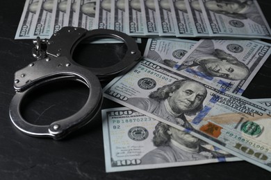 Photo of Corruption. Handcuffs and dollar banknotes on black table, closeup