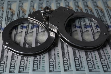 Photo of Corruption. Handcuffs on dollar banknotes, closeup view