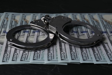 Photo of Corruption. Handcuffs and dollar banknotes on black table, closeup