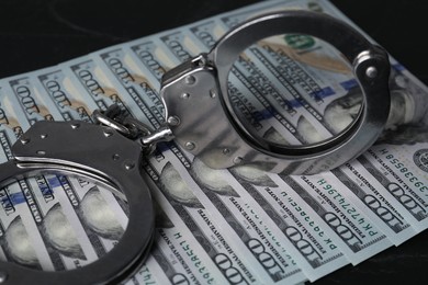 Corruption. Handcuffs and dollar banknotes on black table, closeup