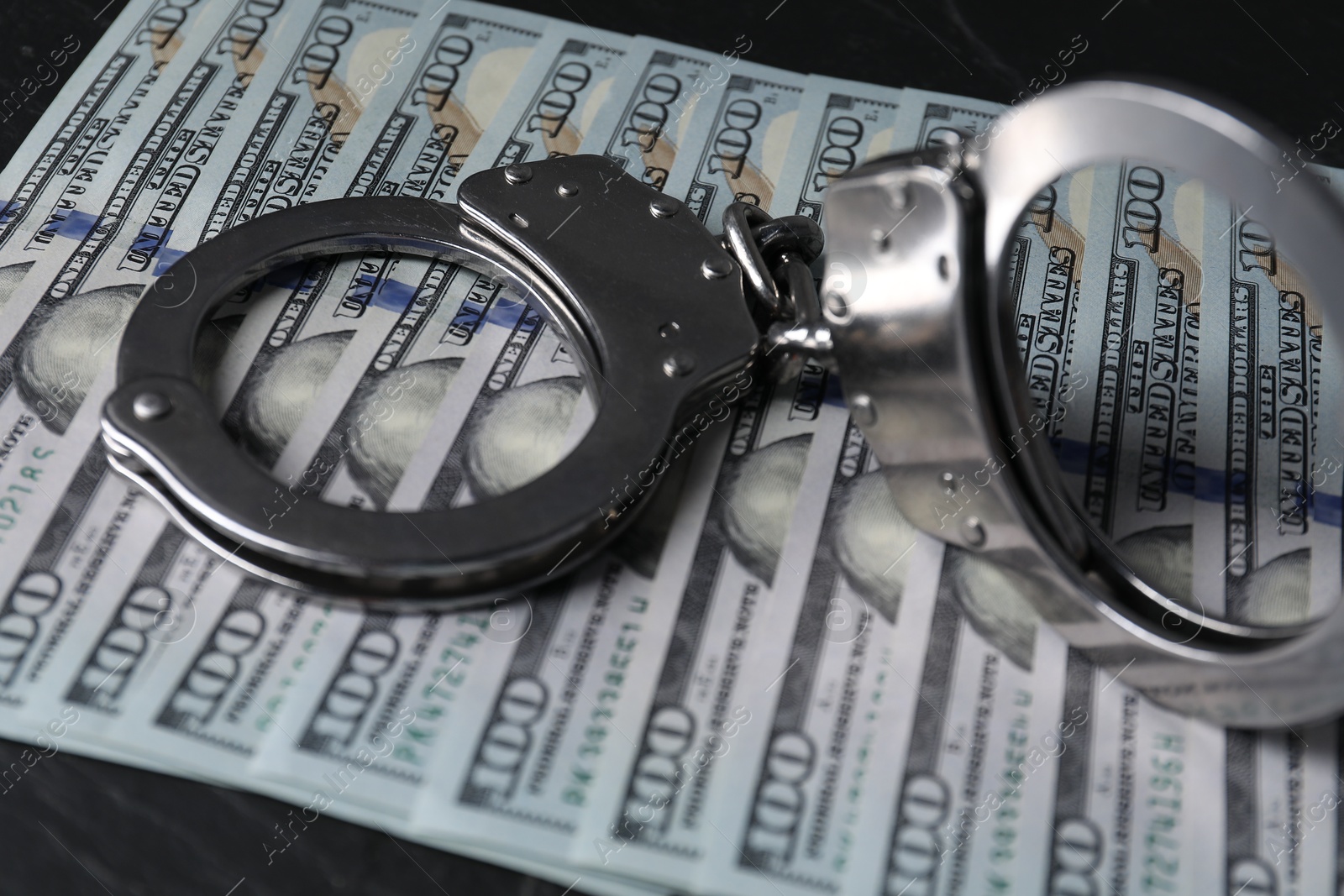 Photo of Corruption. Handcuffs and dollar banknotes on black table, closeup