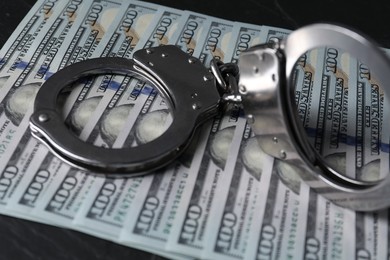 Corruption. Handcuffs and dollar banknotes on black table, closeup