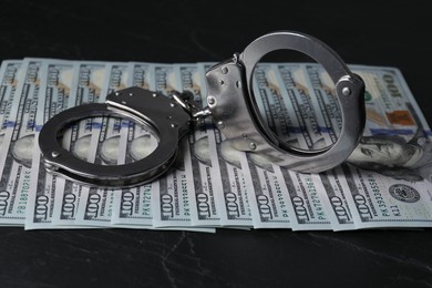 Photo of Corruption. Handcuffs and dollar banknotes on black table, closeup