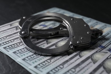 Corruption. Handcuffs and dollar banknotes on black table, closeup