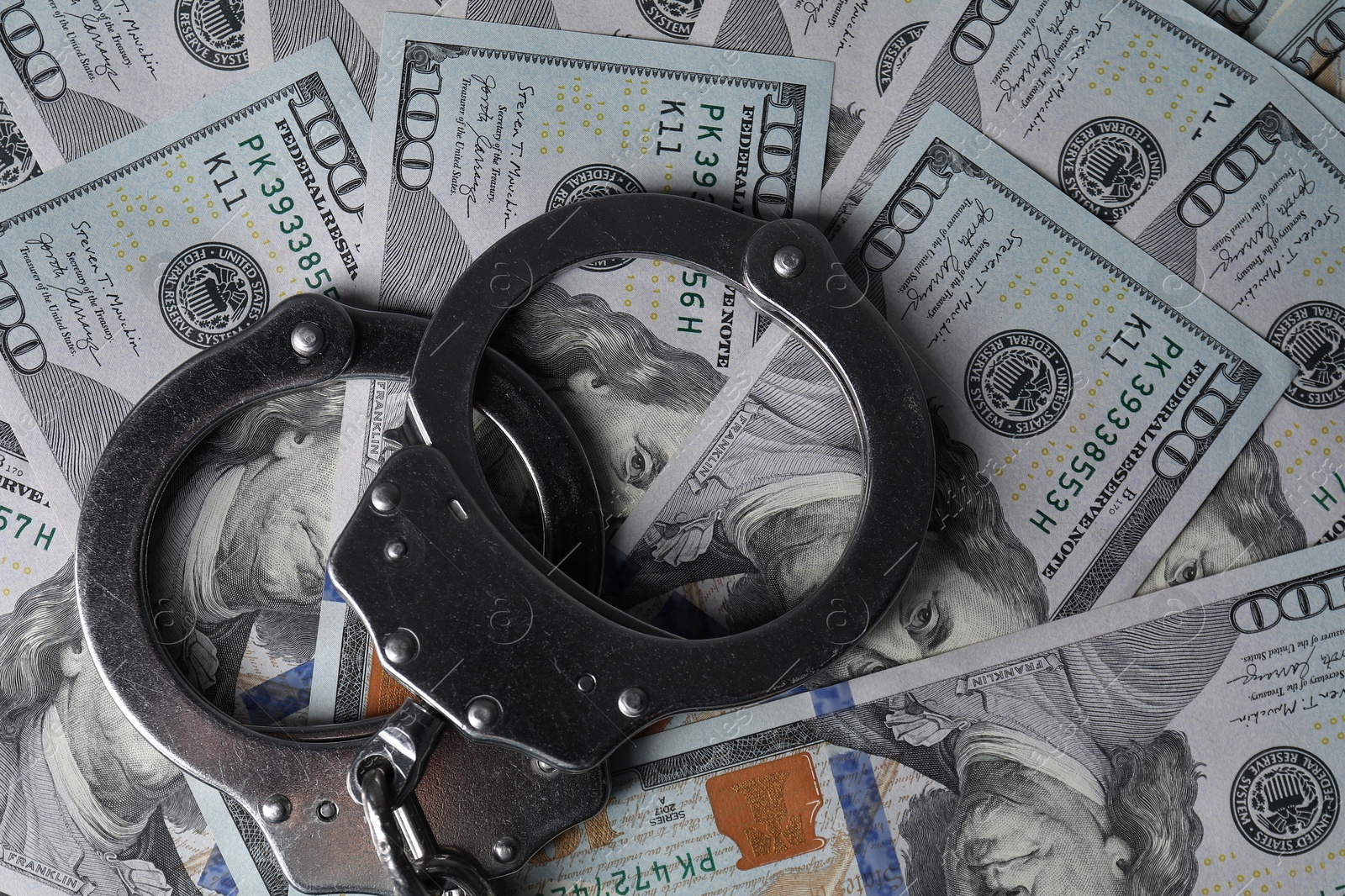 Photo of Corruption. Handcuffs on dollar banknotes, top view