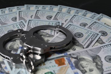 Photo of Corruption. Handcuffs and dollar banknotes on black table, closeup