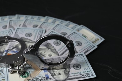 Photo of Corruption. Handcuffs and dollar banknotes on black table, closeup